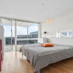 Schlafzimmer mit Balkon, Bett und Holzboden. Fenster und Tür bieten Blick auf Außenbereich.