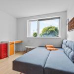Ein Zimmer mit blauem Sofa, Schreibtisch und Fenster mit Blick auf Bäume.
