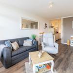 Wohnzimmer mit Sofa, Sessel und Couchtisch. Küche im Hintergrund.