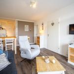 Wohnbereich mit Sofa, Sessel, Esstisch und Fernseher an der Wand.