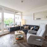 Wohnzimmer mit Sofa, Sessel und Terrasse. Holzfußboden und große Fenster.