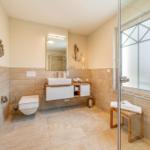 Badezimmer mit Dusche, Waschbecken und Toilette. Wandverkleidung aus Stein und Holz.