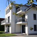 Modernes Haus mit Balkonen und grünem Grundstück.