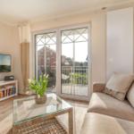 Wohnzimmer mit Sofa, Glas-Tisch und Balkontür. Fernseher und Bücherregal sichtbar.