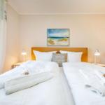 Zwei Betten mit weißen Bettwäschen und Handtüchern. Wandbild und Spiegel sind sichtbar.