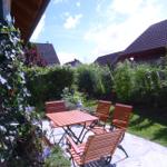 Terrasse mit Holztisch und Stühlen, umgeben von Grün und Häusern.