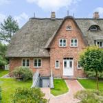 Rotes Backsteinhaus mit Strohdach und weißer Eingangstür. Grün umgeben mit gepflastertem Weg.