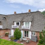 Haus mit strohgedecktem Dach und Balkonen. Gartenbereich mit Tischen und Stühlen.