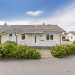 Ein hellfarbenes Haus mit Garten und gepflastertem Weg. Hintergrund: weitere Häuser und Straße.