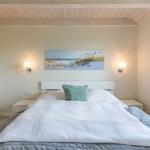 Schlafzimmer mit Bett, Wandbild und Stehlampen.