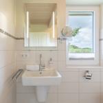 Badezimmer mit Waschbecken, Spiegel und Fenster mit Blick auf Grünflächen.