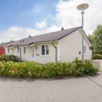 Ein hellbeiges Haus mit Dach und Fenstern. Umgeben von Grünflächen und einem Gehweg.