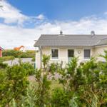 Ein weißes Ferienhaus mit Garten und Terrasse unter blauem Himmel.
