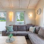 Wohnzimmer mit Ecksofa, Holztisch und Fenstern.