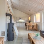 Wohnzimmer mit Esstisch, Küche und Kaminofen unter Holzdecke.