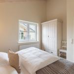 Schlafzimmer mit Bett, Kleiderschrank und Fenster. Tür und Stuhl sind sichtbar.