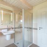 Badezimmer mit Dusche, Waschbecken und Spiegel unter Holzbalkendecke