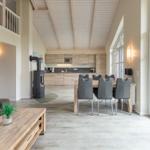 Wohn- und Essbereich mit Küche und Terrasse. Holzdecke und große Fenster.