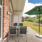 Terrasse mit Tisch, Stühlen und Sonnenschirm. Hinterhof mit Liegestühlen und Grünflächen.