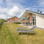 Haus mit Garten, Liegestühlen und Terrasse unter grünem Sonnenschirm.