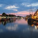 Hafen bei Dämmerung mit Booten und beleuchteten Gebäuden.