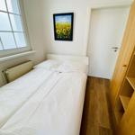 Schlafzimmer mit Bett, Holzregal und Fenster. Wandbild zeigt Sonnenblumen.