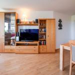 Wohn- und Essbereich mit Holzmöbeln, TV und Balkonzugang.