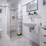 Badezimmer mit Dusche, Waschbecken und Toilette. Weiße Fliesen und blauer Akzent.