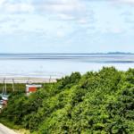 Meeresblick mit Strand, Booten und grüner Vegetation im Vordergrund.