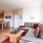 Wohnbereich mit Sofa, Couchtisch und Essbereich. Küche im Hintergrund.