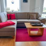 Ein Wohnzimmer mit grauem Sofa, rotem Teppich und Holztisch.