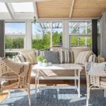 Sitzbereich mit Wickerstühlen und Sofa unter Glasdach mit Blick auf Garten.