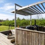 Holzterrasse mit Grill, Feuerkorb und Pavillon. Grünflächen und Bäume im Hintergrund.