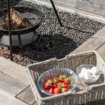 Feuerkorb mit Grillrost, Körbchen mit Erdbeeren und Marshmallows auf Holzterrasse.