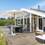 Terrasse mit Tisch, Stühlen und Sonnenschirm. Hintergrund: Haus mit Glasfront und Garten.