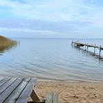 Holztisch am Strand mit Blick auf einen Steg ins Wasser.