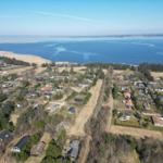 Luftbild einer Küstenlandschaft mit Häusern und einem großen Gewässer im Hintergrund.