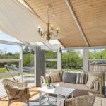 Terrassenbereich mit Sofa, Stühlen und Tisch unter Holzdecke mit Blick auf Garten.