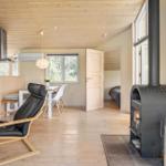 Holzvertäfelte Küche mit Esstisch, Sessel und Kaminofen. Schlafzimmer im Hintergrund.