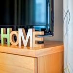 Holzfiguren mit dem Wort HOME stehen vor einem Fernseher auf einem Schrank.