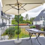 Terrasse mit Tisch, Stuhl und Sonnenschirm. Blick auf Wohnhäuser und Grünflächen.