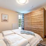 Schlafzimmer mit Doppelbett, Holzschrank und Fenster zum Balkon.