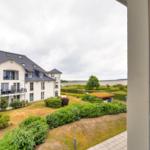 Blick auf ein weißes Gebäude mit Balkonen und grüne Gärten im Vordergrund.