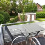 Terrasse mit Tisch und Stühlen, Blick auf grünen Garten und kleines Gebäude.
