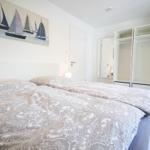 Schlafzimmer mit Doppelbett, Kleiderschrank und Wandbild mit Segelbooten.