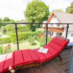 Roter Liegestuhl auf Balkon mit Blick auf Garten und Haus.