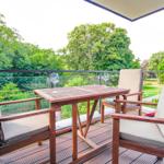 Terrasse mit Holztisch und Stühlen, Blick auf grüne Bäume und Rasen.