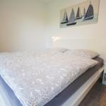 Schlafzimmer mit Doppelbett, Nachttisch und Wandbild mit Segelbooten.