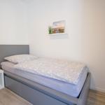 Schlafzimmer mit Bett, Nachttisch und Wandregal mit Bild und Pflanze.