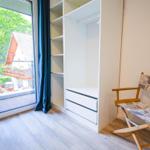 Zimmer mit Garderobe, Stuhl und Balkonblick auf Haus und Grün.